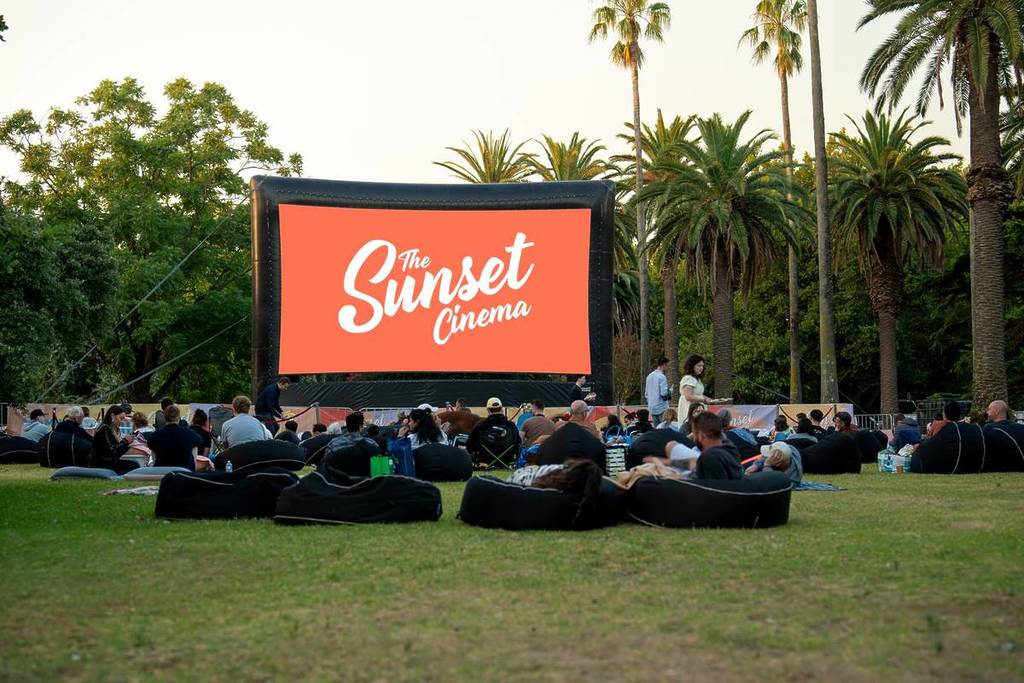 people in the St Kilda Botanical Gardens looking at a screen that says Sunset Cinema