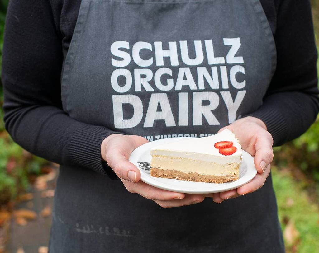 staff member wearing a Schulz Organic Dairy apron and holding a cheesecake