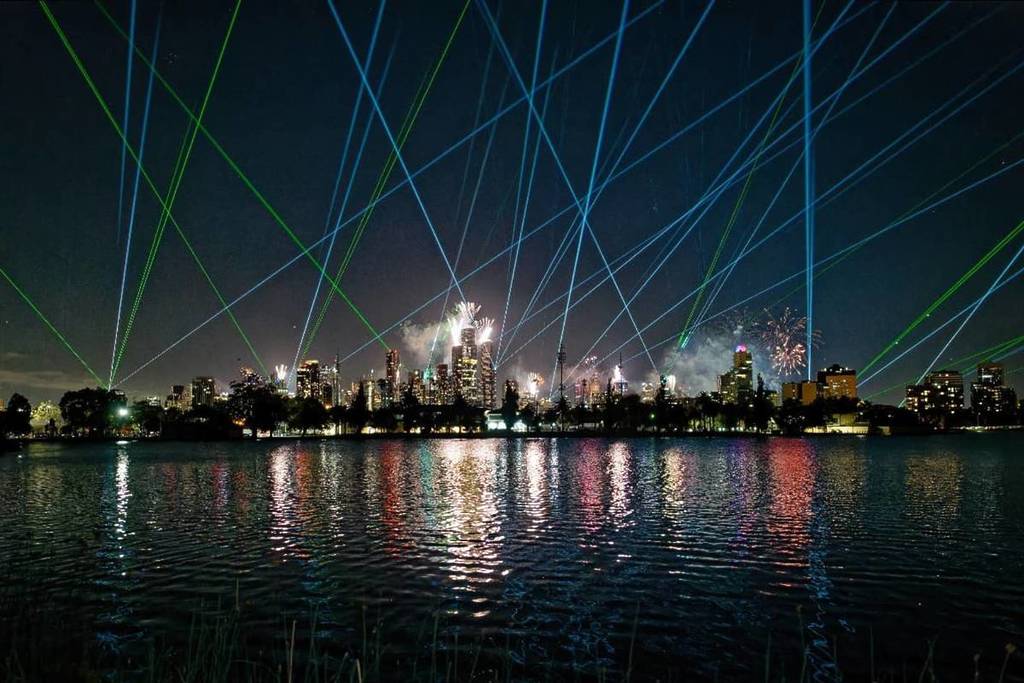 lasers and fireworks over the Melbourne skyline, with a view from over a nearby lake at night