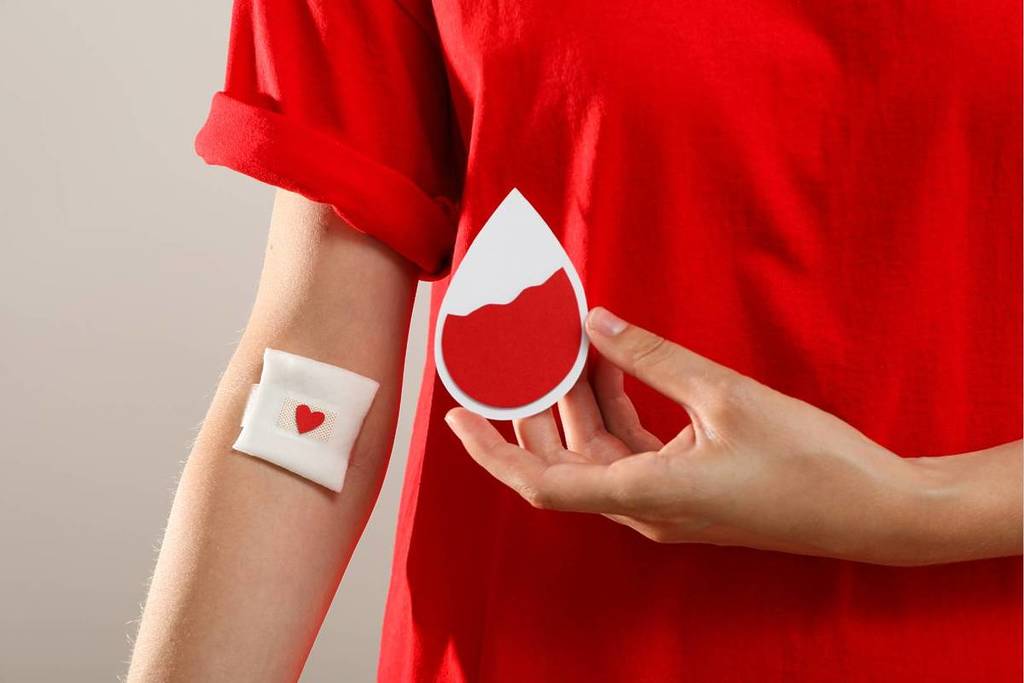 person in red with a bandage on arm holding a sign shaped like a drop of blood