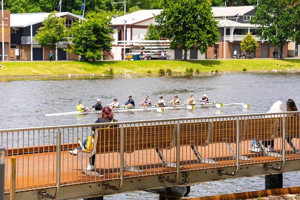 woman on bench in Birrarung Marr watching a rowing team go by
