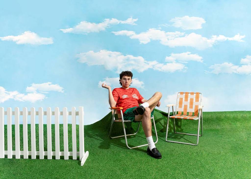 Young Franco on an outdoor chair against a painted backdrop of a sky and grass