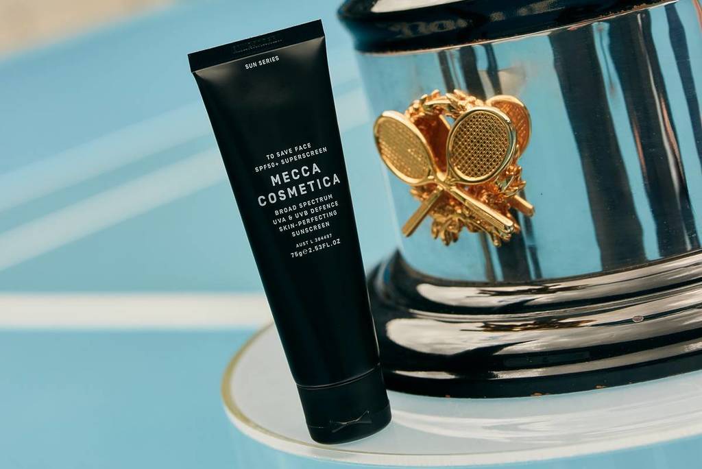 sunscreen from MECCA on a tennis court next to the bottom of a tennis trophy