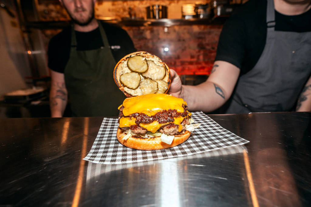 bun lifted off a burger at Arcane Fairies to reveal pickles, cheese and other ingredients
