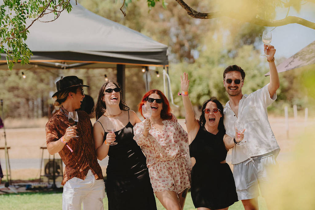 A group of people with wine glasses in their hands pose for a photo outside at Tastes of Rutherglen.