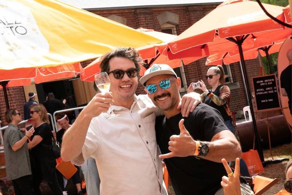 two men smiling for camera holding glass of prosecco at festival