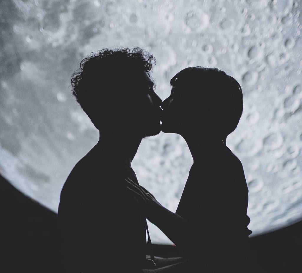 two people kissing in front of a full moon