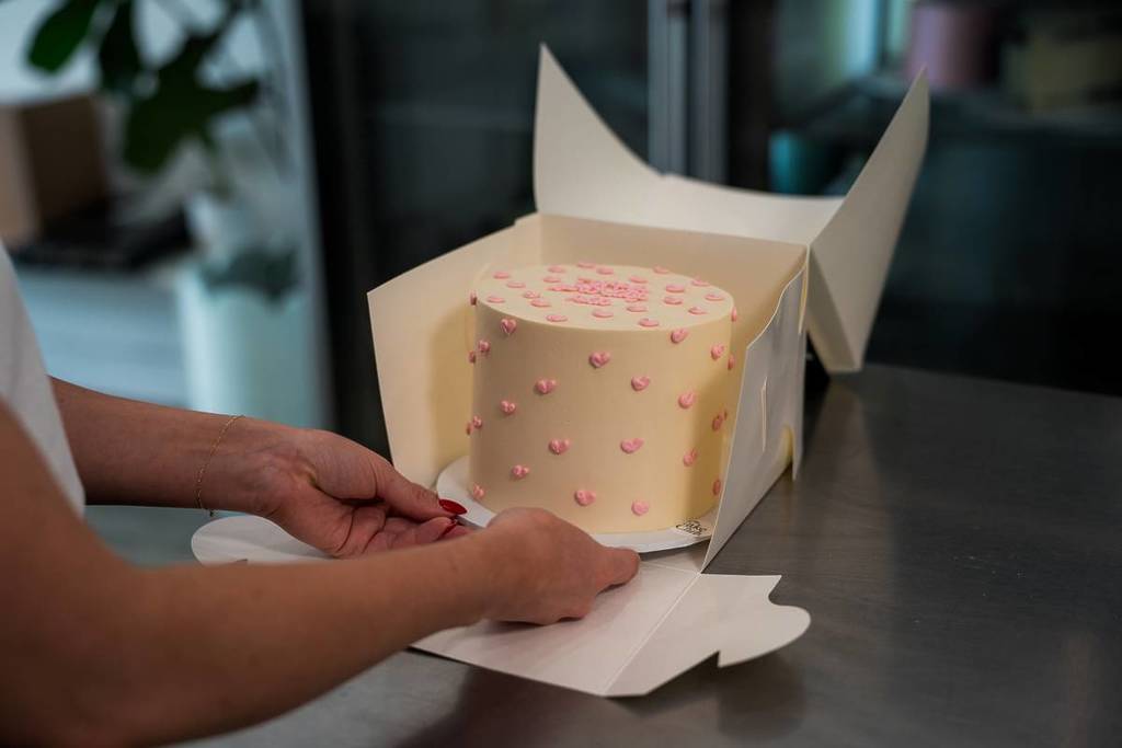 woman putting cake with buttercream pink hearts in a box from The Cake Club