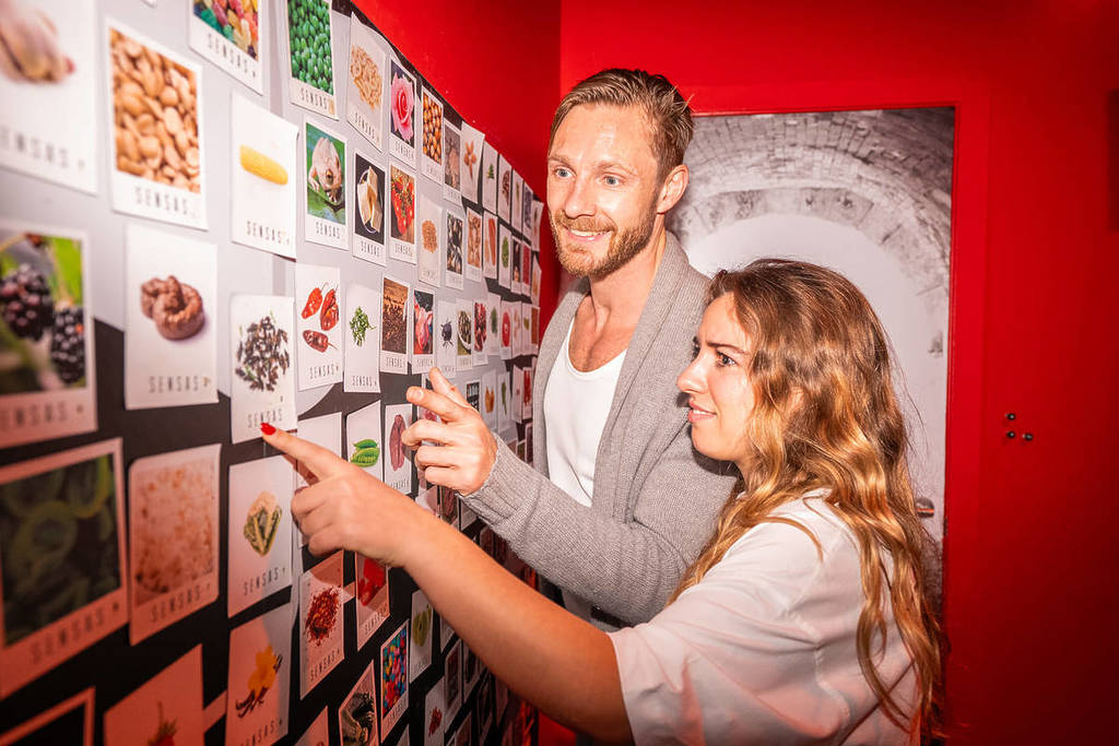 A man and a woman look at photos on a wall of different foods that they may have tried in the Taste Lab at SENSAS.