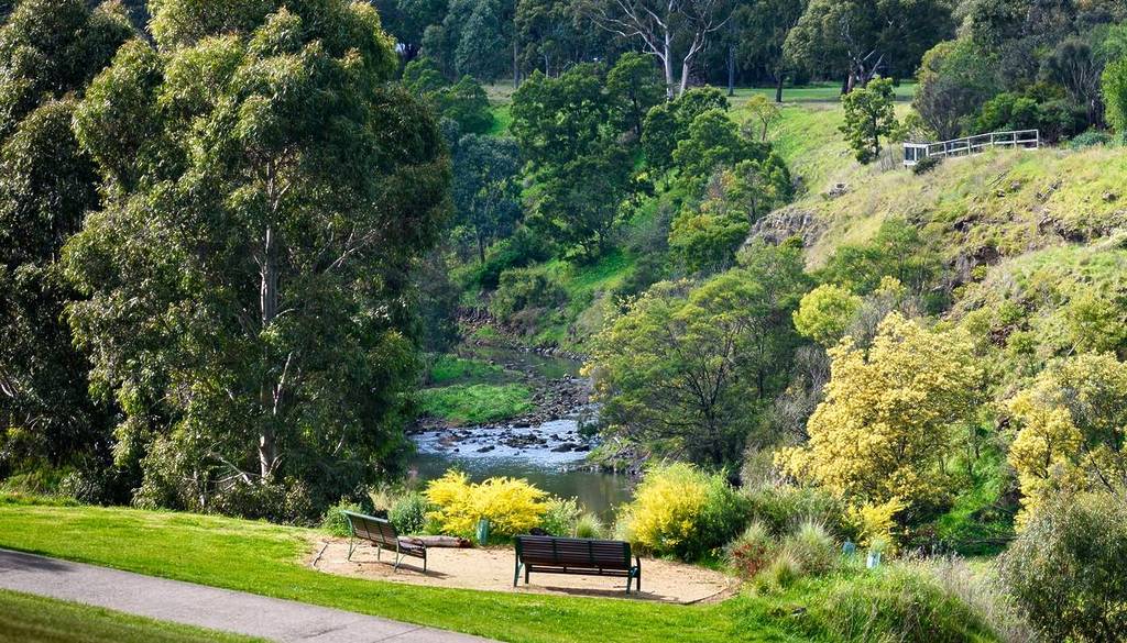 view of Merri Creek, with a park bench and a flat trail in the foreground