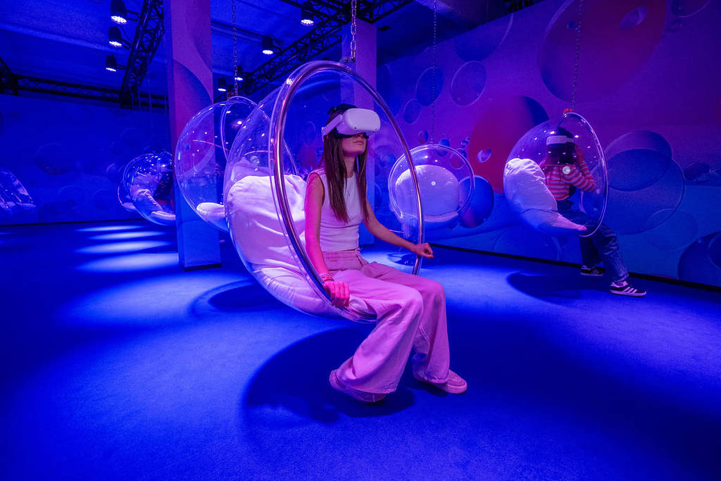 A woman with a VR headset on sits in a bubble chair hanging from the ceiling at Bubble Planet. 
