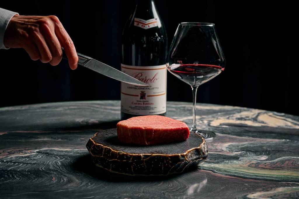 piece of wagyu from Steer Dining Room on a decorative wood display, with a glass of wine and bottle in the background