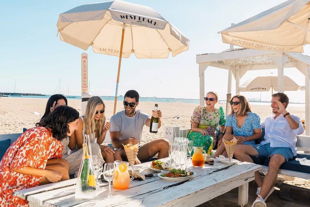 group of people around a table under umbrellas on a beach at West Beach Pavilion in St Kilda