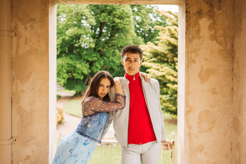 man and woman in vintage clothes posing in a doorway with a garden behind them, showcasing items that could be on displace at the Vintage Clothing & Collectables Sale