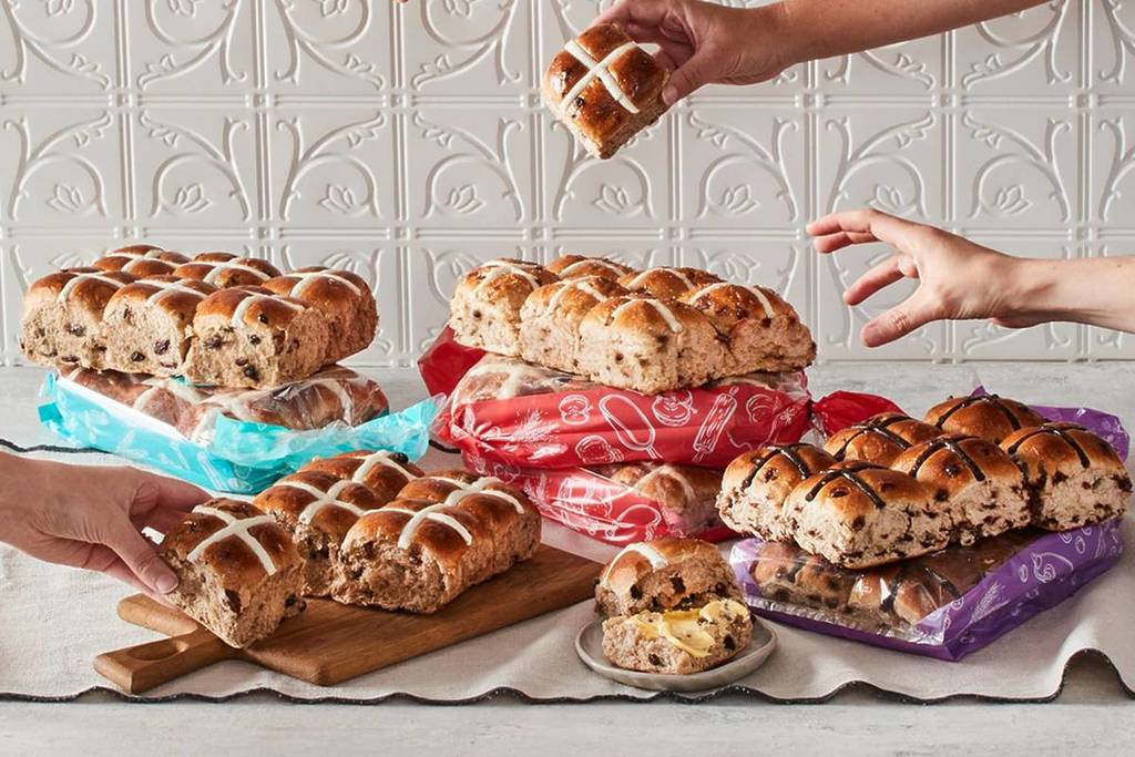hands reaching out to grab one of three kinds of hot cross buns available at Bakers Delight