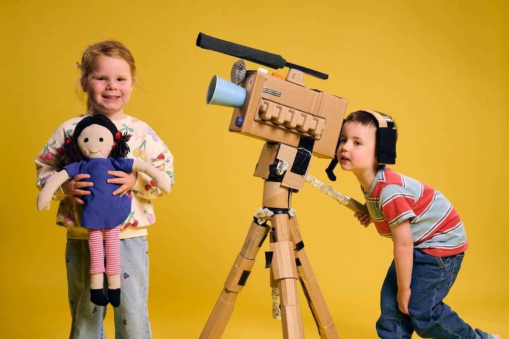 boy pretending to be a camera operator and girl holding a doll and pretending to be a presenter