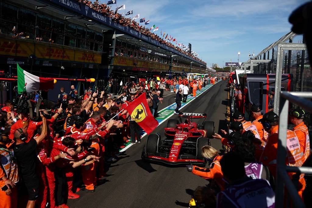ferrari sports car at the grand prix, with fans cheering from the grand stand, and pit crew welcoming the car with flags