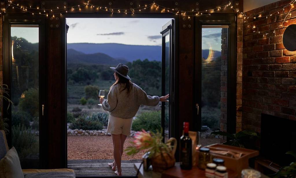 woman holding a glass of wine looking out at a view of the Grampians in the doorway of the Nook on the Hill accommodation