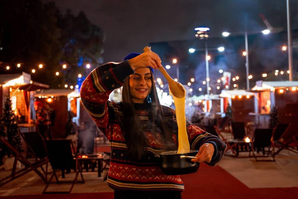 woman in the Fondue Chalet alpine village, using a spoon to lift up a melted cheese from a pot