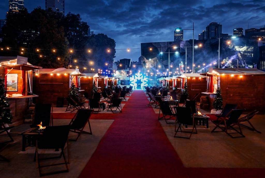 outside the different wooden chalets at Fondue Chalet, with a red carpet in the centre leading to a neon snowflake installation