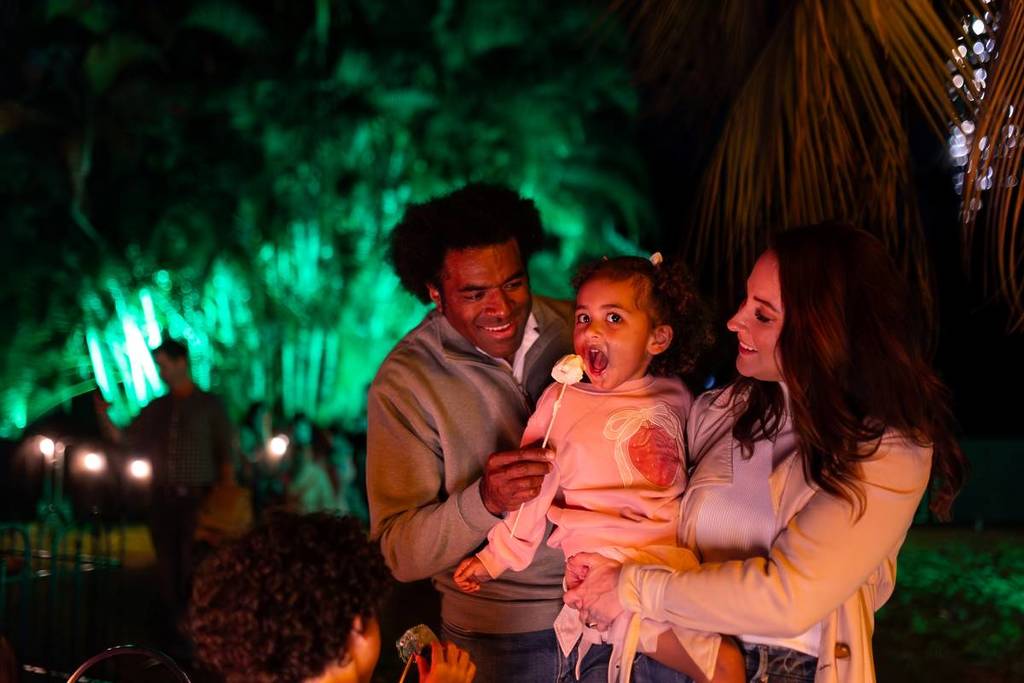 two parents holding a toddler and a roasted marshmallow at Lightscape