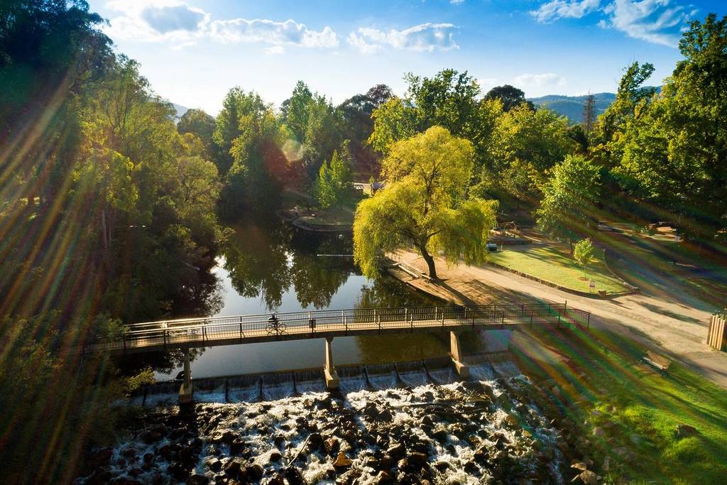 aerial view of a bridge over the Ovens River in Bright, with someone cycling over it on a sunny day