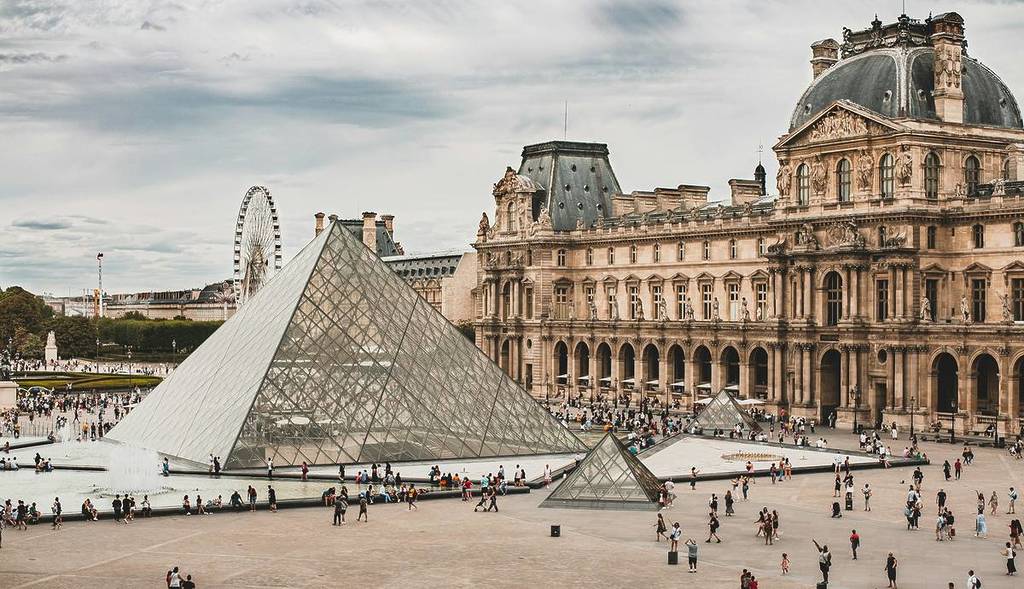 view of the outside of the Louvre with people milling around the famous glass pyramid