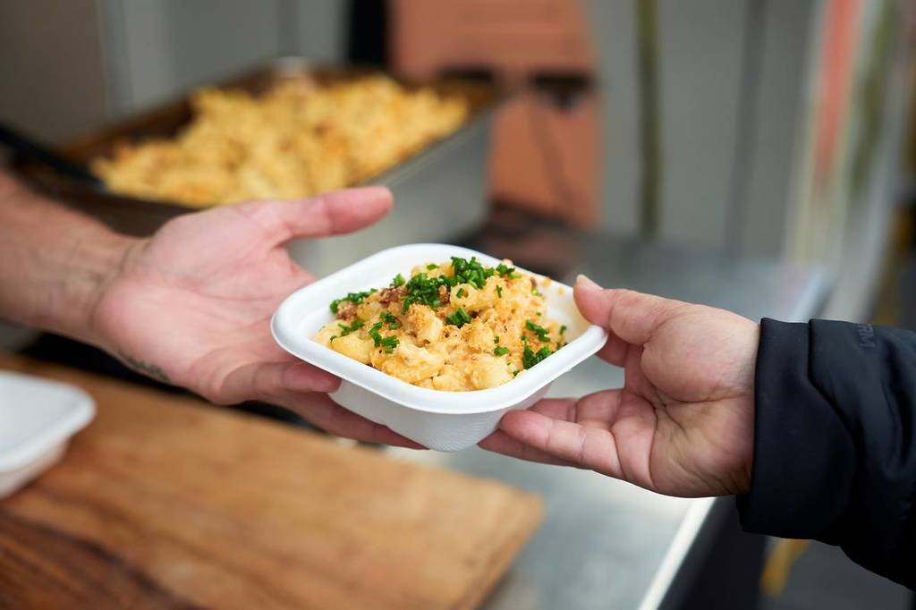 hand passing a bowl of mac and cheese to another hand at Prahran Market