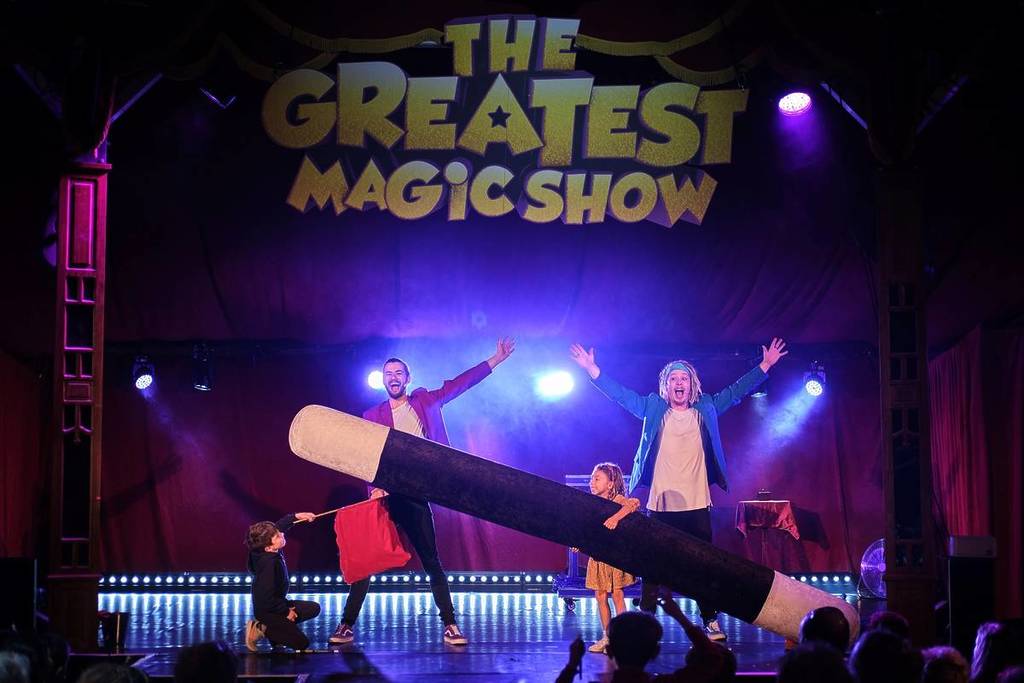 children helping magicians hold a wand in a magic show