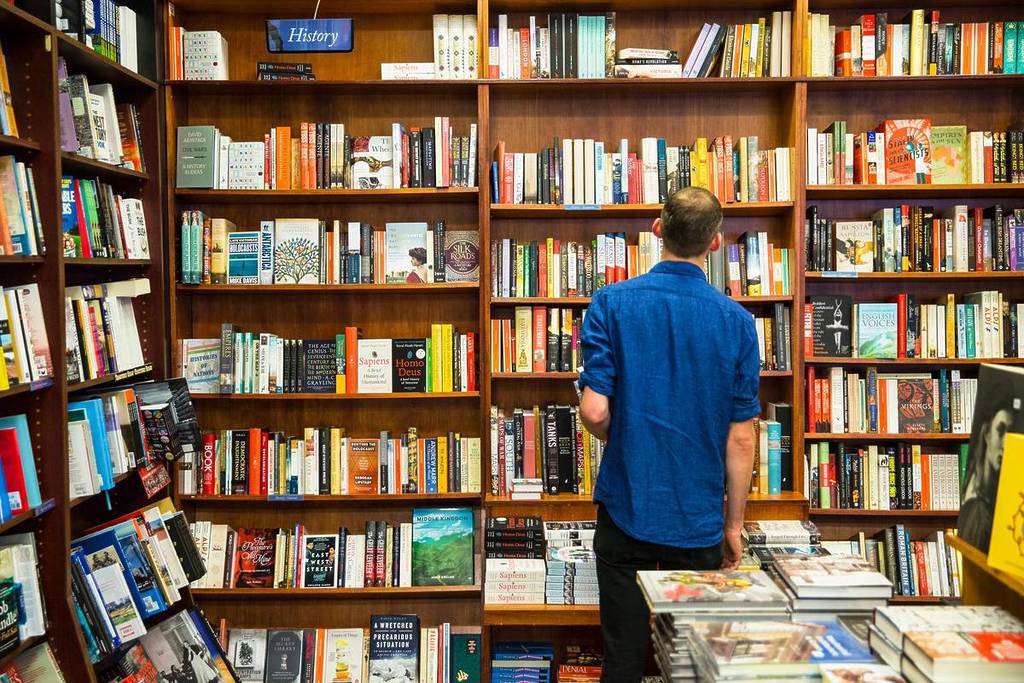 man standing in front of bookshelf at Readings in Carlton