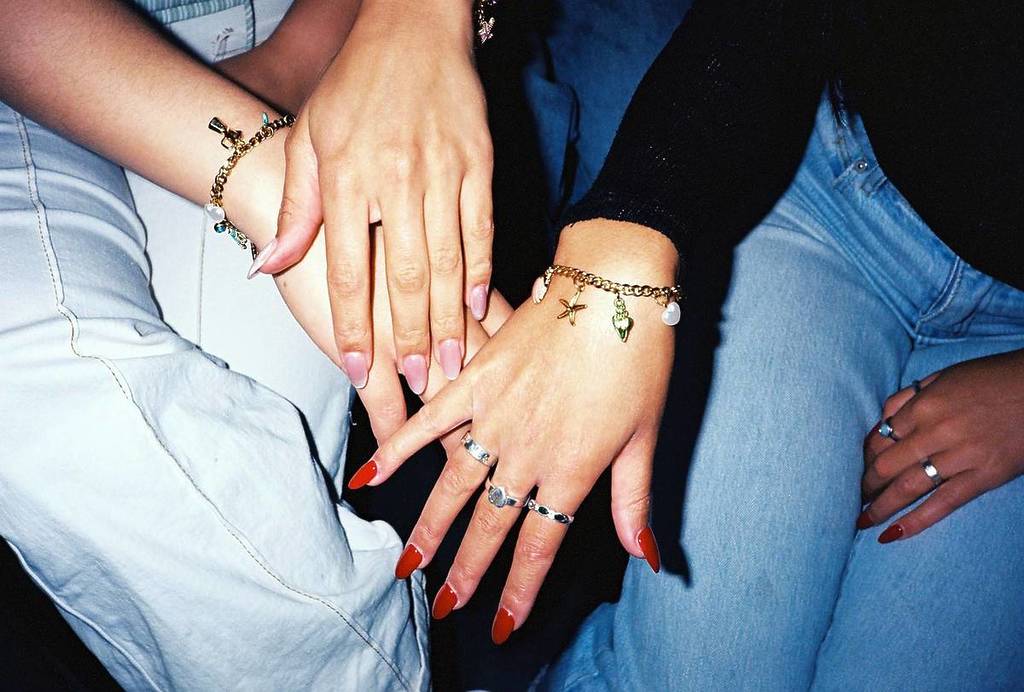 two hands wearing charm bracelets
