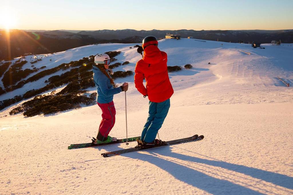 two people skiing on Mt Buller looking towards Mt Stirling during golden hour