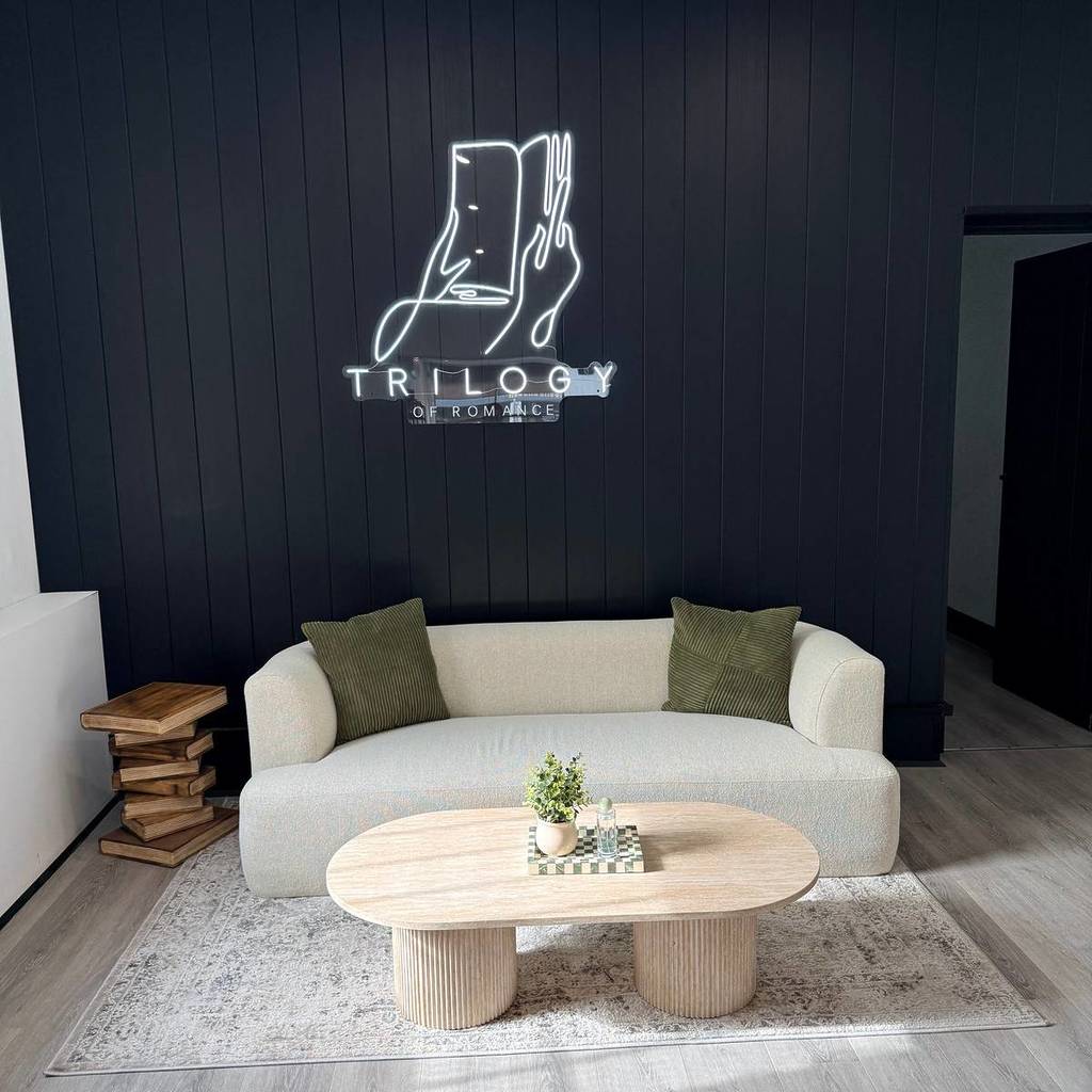 couch against a wall that has a neon sign saying Trilogy of Romance