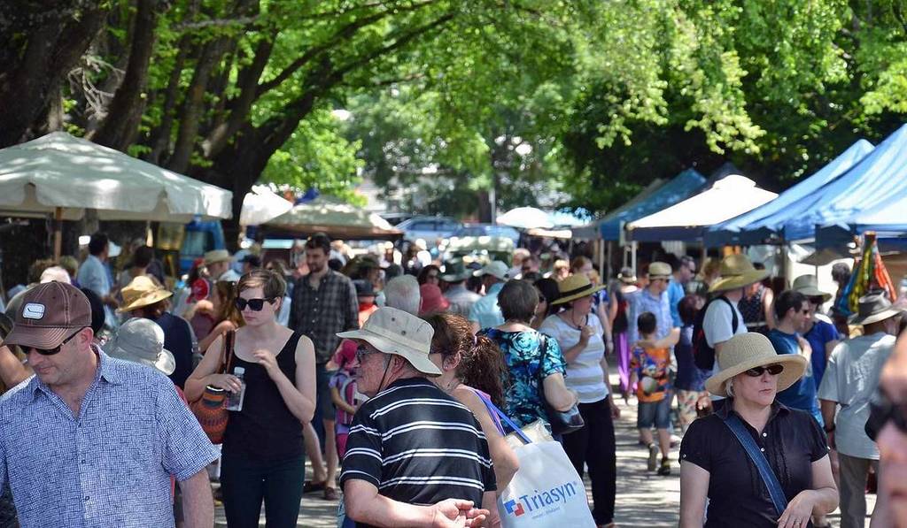 people walking past stalls under leafy green trees at Daylesford Sunday Market