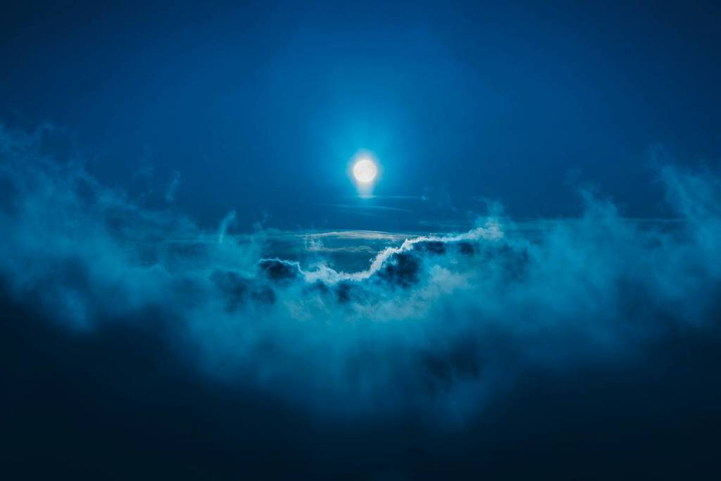 a full moon on a blue night, seen from far away, with clouds in the foreground