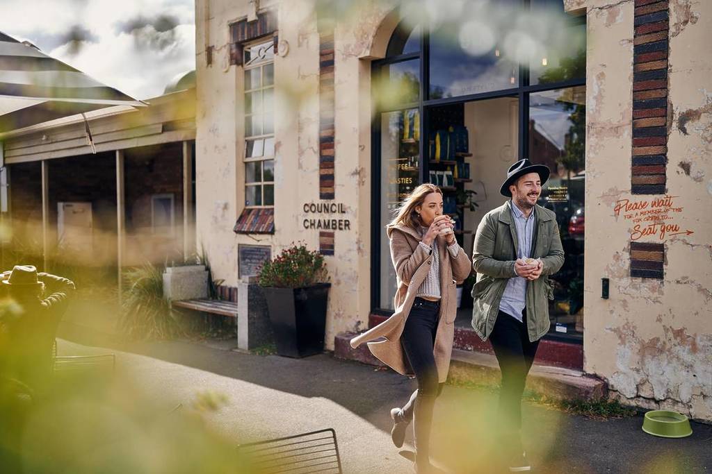 woman sipping coffee next to man as they walk down a street in Woodend
