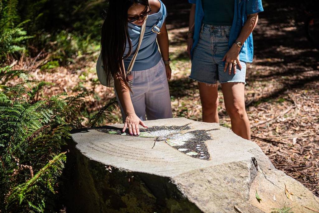 two women looking at a mosaic of a butterfly on a boulder on the Ngarruk Barring trail