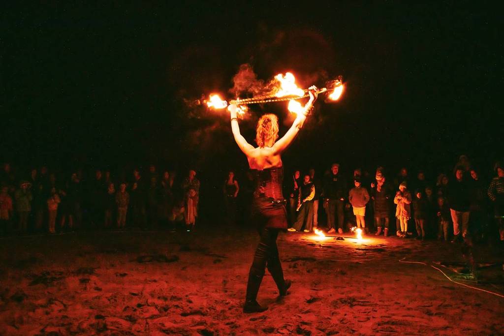 fire performer holding up a burning stick prop at Nightide