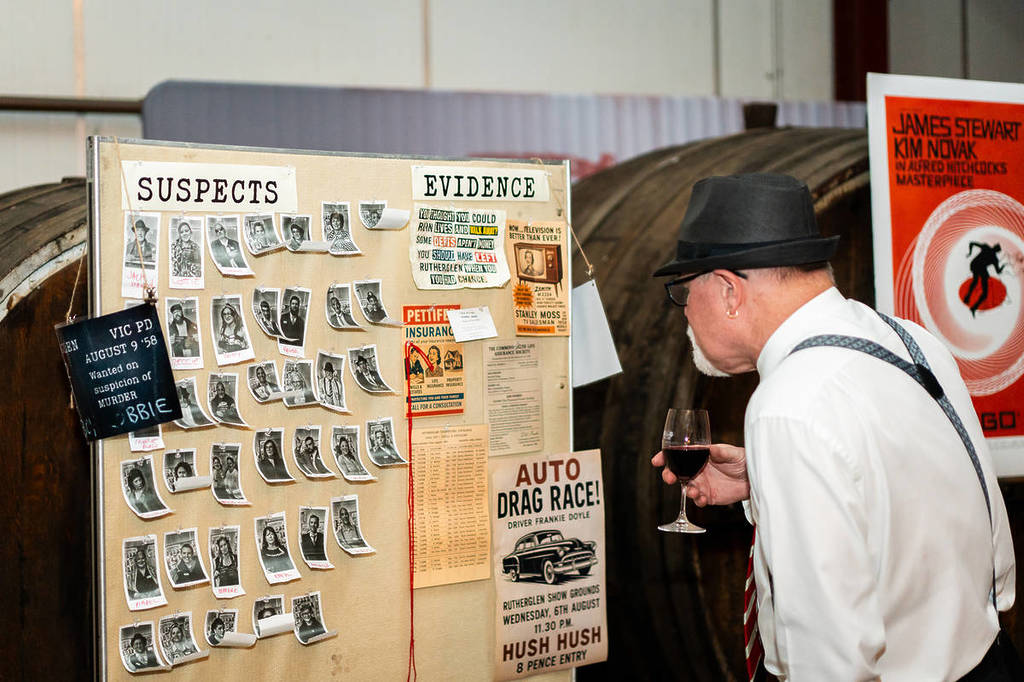 A man looks at a corkboard with photos of suspects and evidence at the Murder Mystery event at Dark Side of Wine.