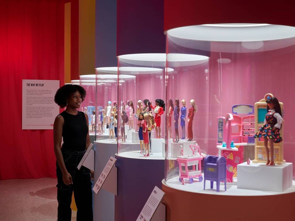 woman in museum looking at displays full of Barbie dolls and furniture