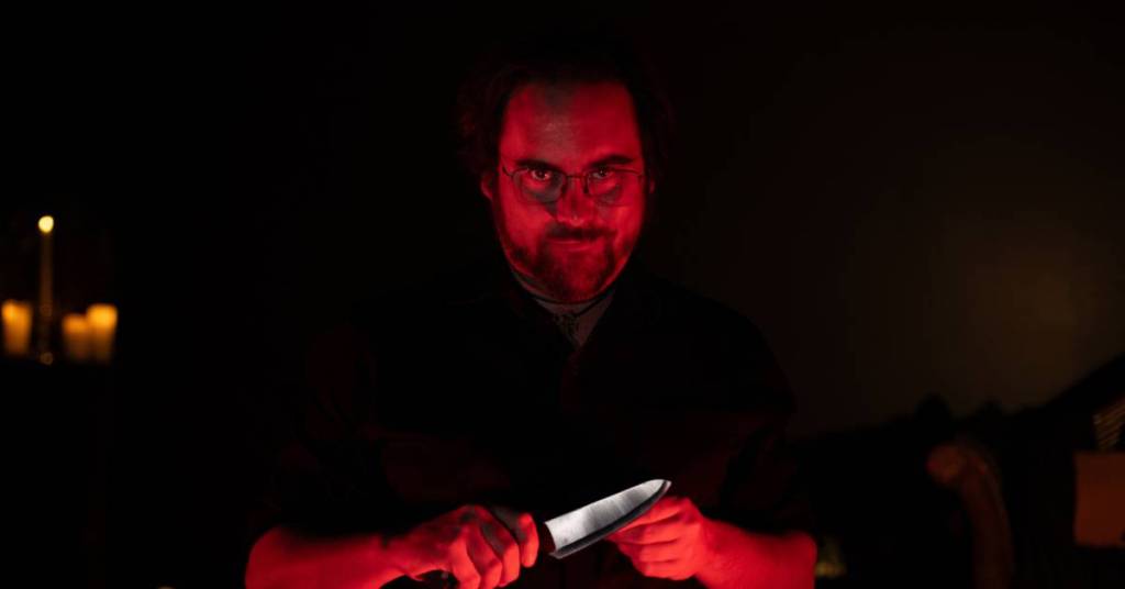 An actor in a dim-lit room holding a knife
