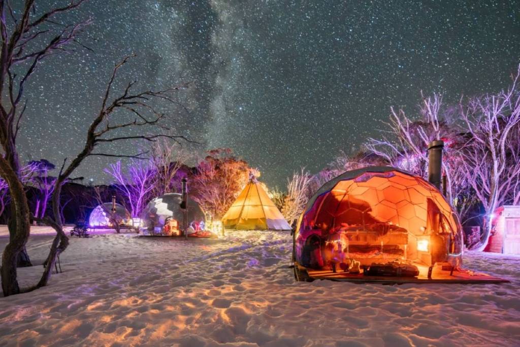 three Hypedomes and a tipi in the snow on Mount Hotham, with the night sky filled with stars, as part of the overnight glamping adventure from Alpine Nature Experience