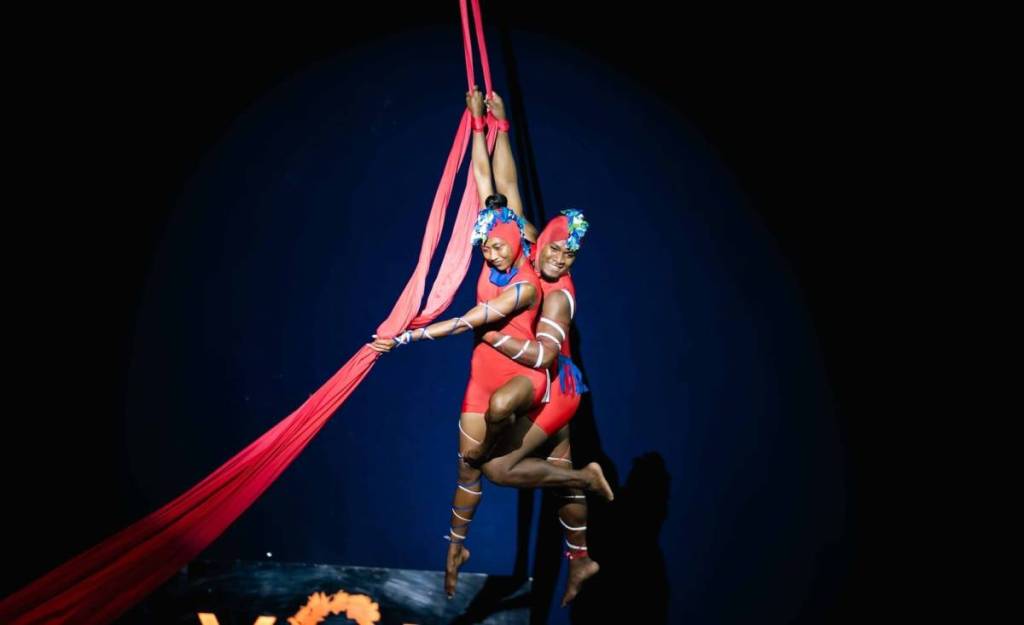 Two performers dressed in red costumes perform an acrobatic aerial stunt at the Fijian Flying Circus Tour.
