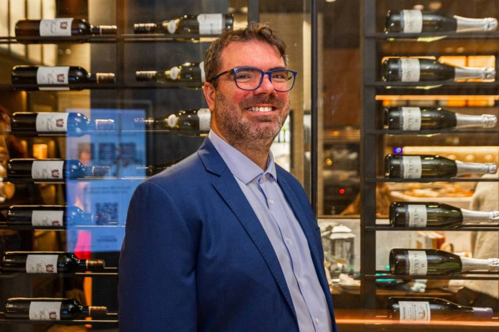 Alex Charasse smiling in front of wine bottles at Almost French Epicure