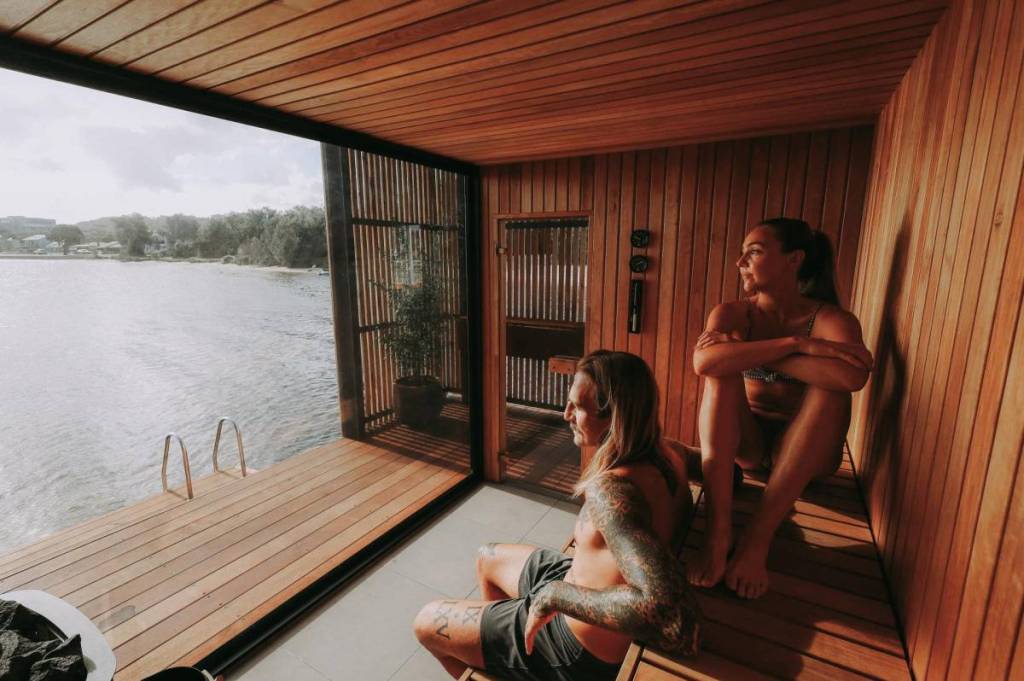 two people relaxing in Koho Floating Sauna and looking out at the lake