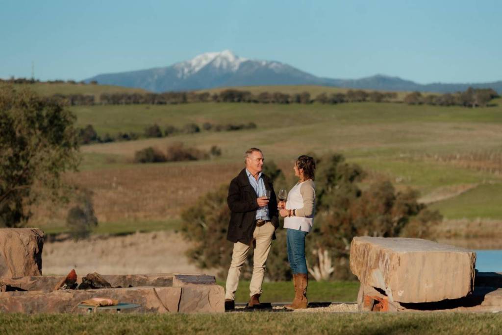 two people sipping wine outdoors at Delatite Winery near Mansfield, with snowy mountain in background