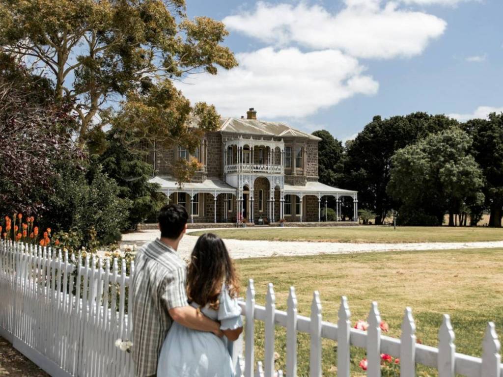 a couple behind a white fence looking towards Barwon Park Mansion