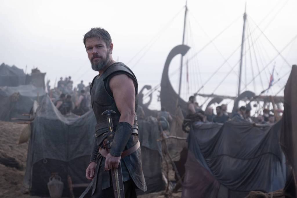 still from The Odyssey, with Matt Damon on a beach with a boat in the background