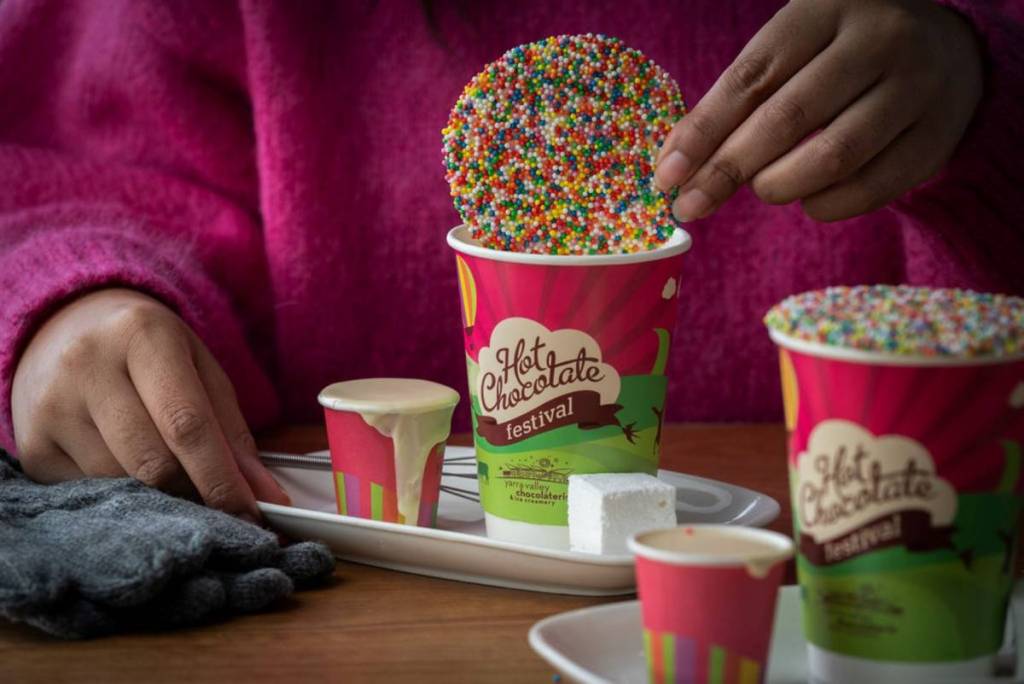 sprinkled covered chocolate disc being dipped into hot chocolate