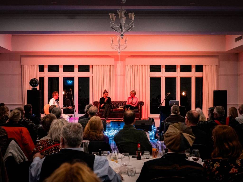 two people on a couch for a talk at Words in Winter, with an audience at dinner tables